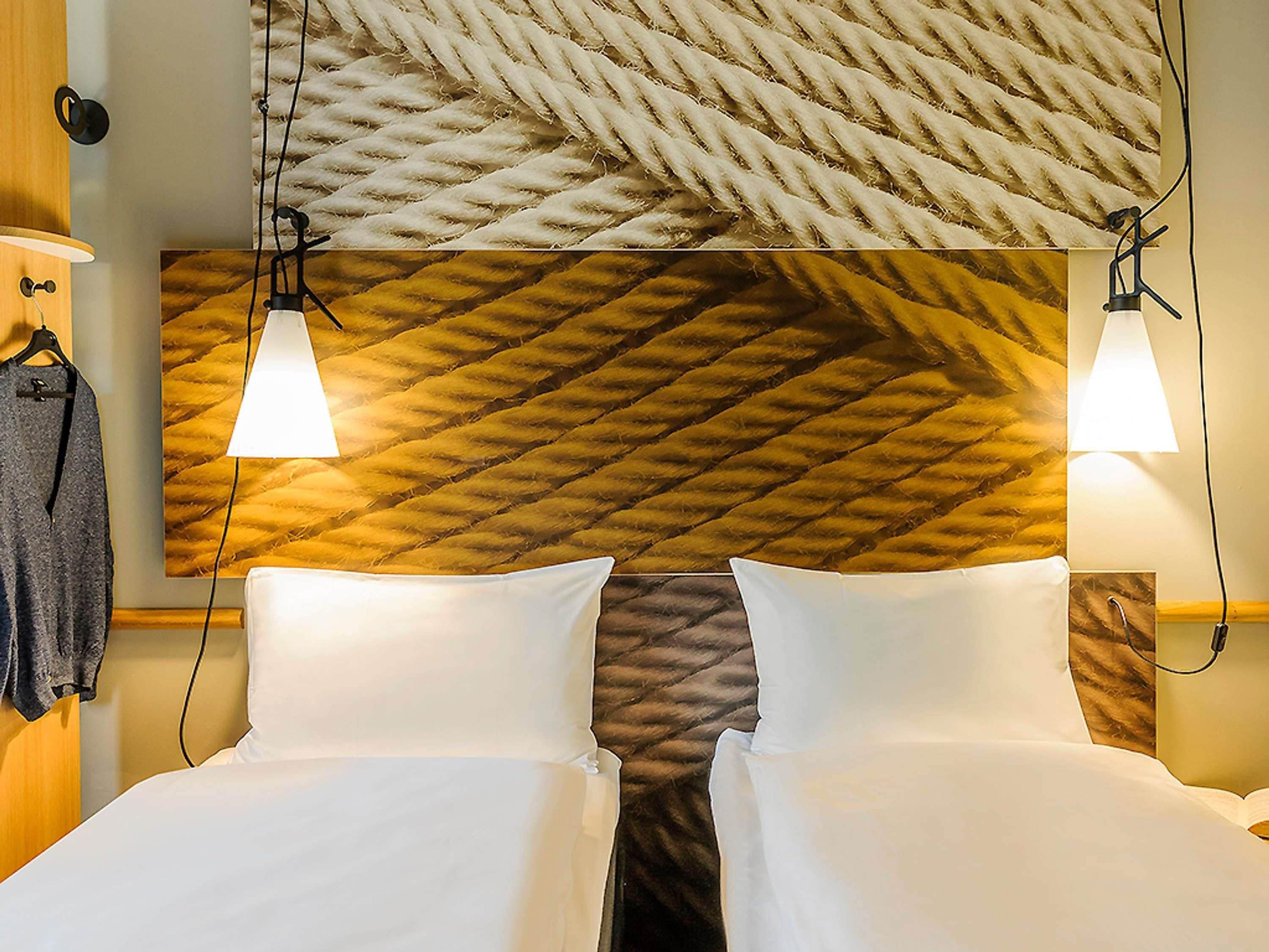 A hotel room with a headboard featuring a textured pattern, two bedside lamps, and a neatly made bed with white linens.