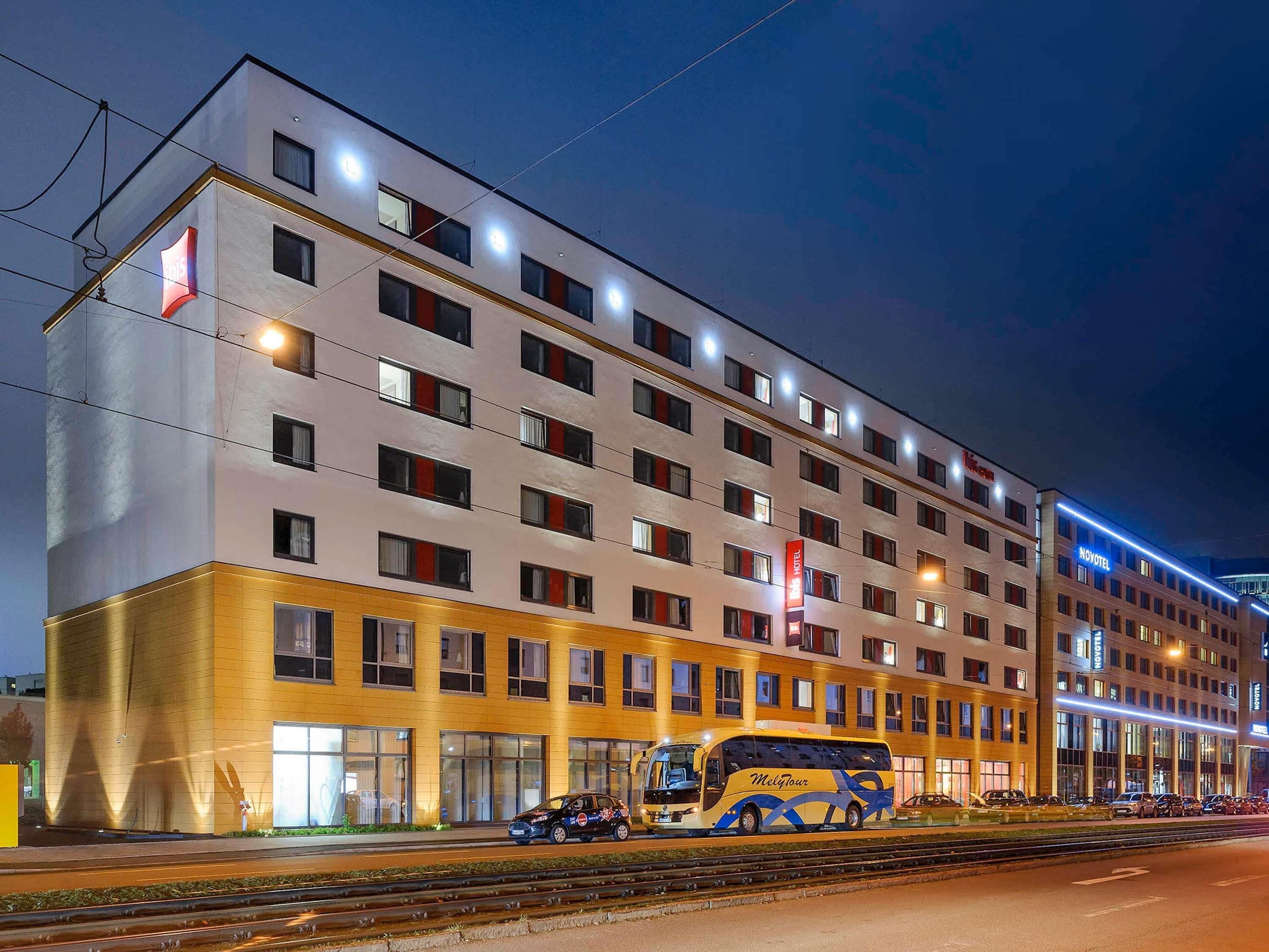 Ein mehrstöckiges Hotel im modernen Stil, mit einem gut sichtbaren Hotelschild, einem Bus vor der Fassade und einem Gleis parallel zum Gebäude.