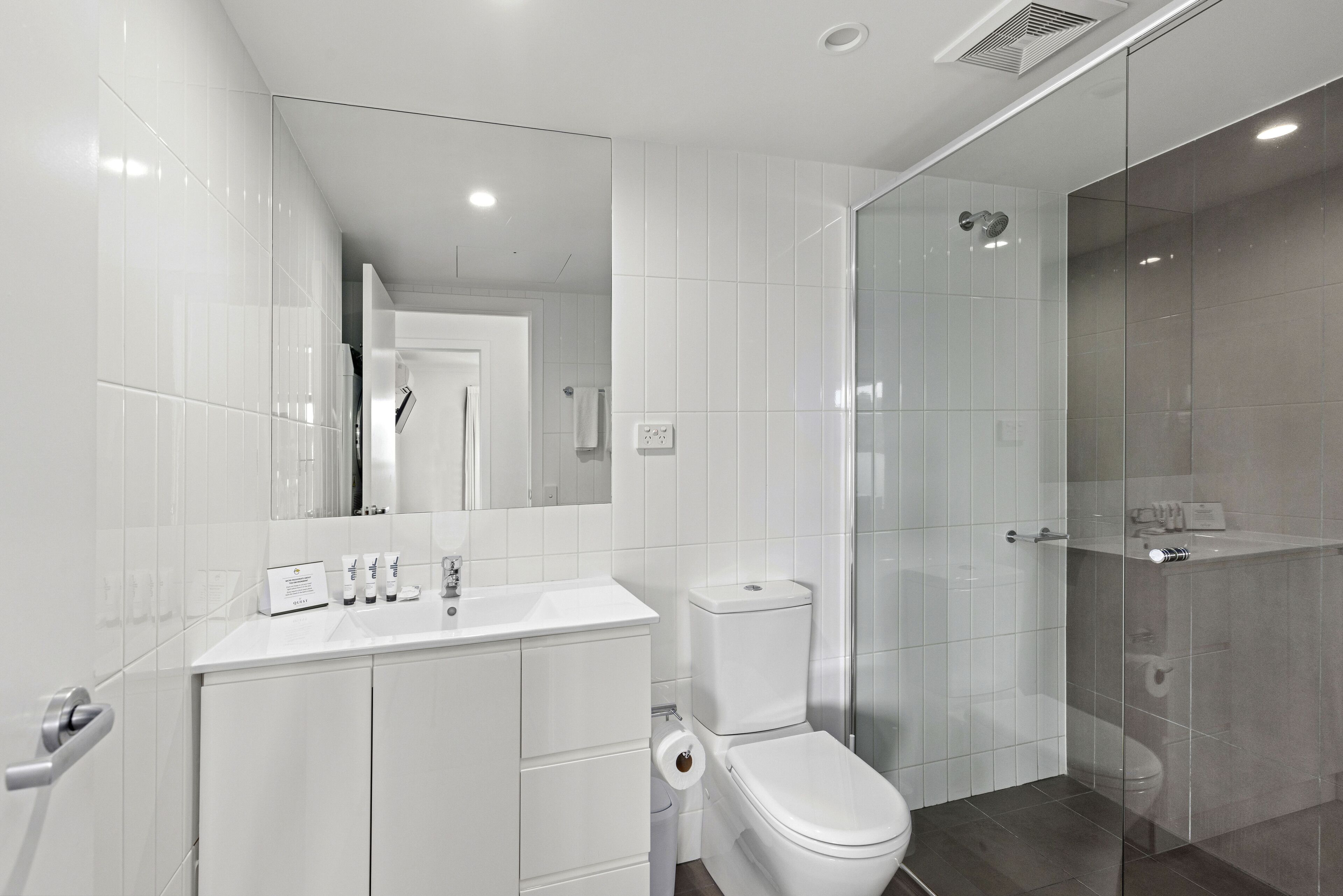 A modern bathroom with a white sink, toilet, and glass shower enclosure.