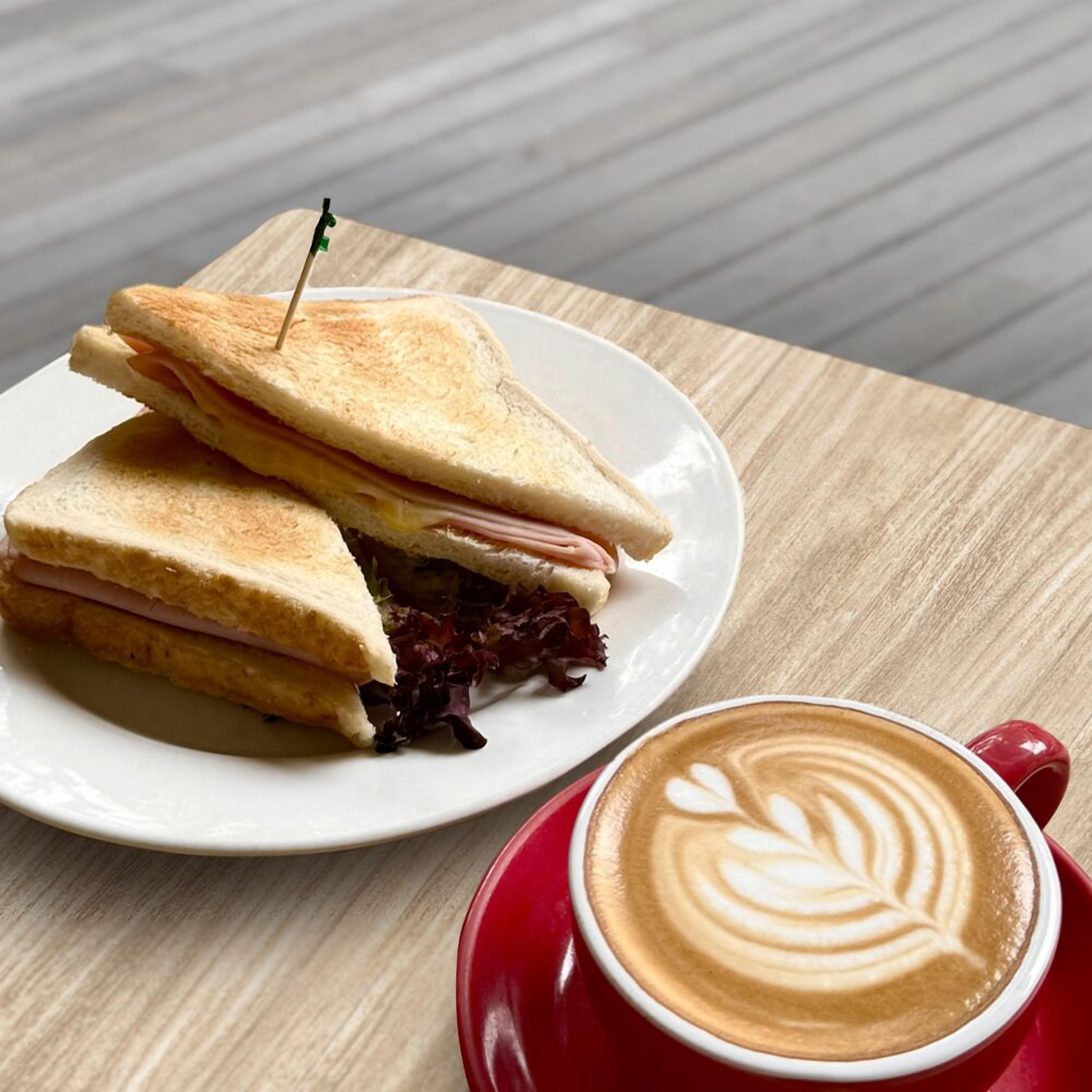 A sandwich on a plate with a red cup of coffee beside it.