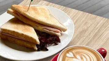 A sandwich on a plate with a red cup of coffee beside it.