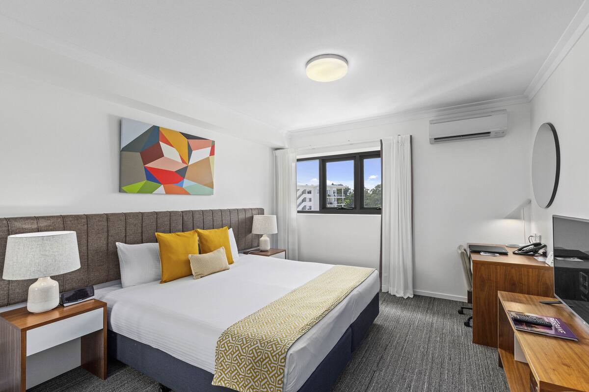 Una habitación de hotel con una cama grande, un escritorio, un televisor y un equipo de aire acondicionado.
