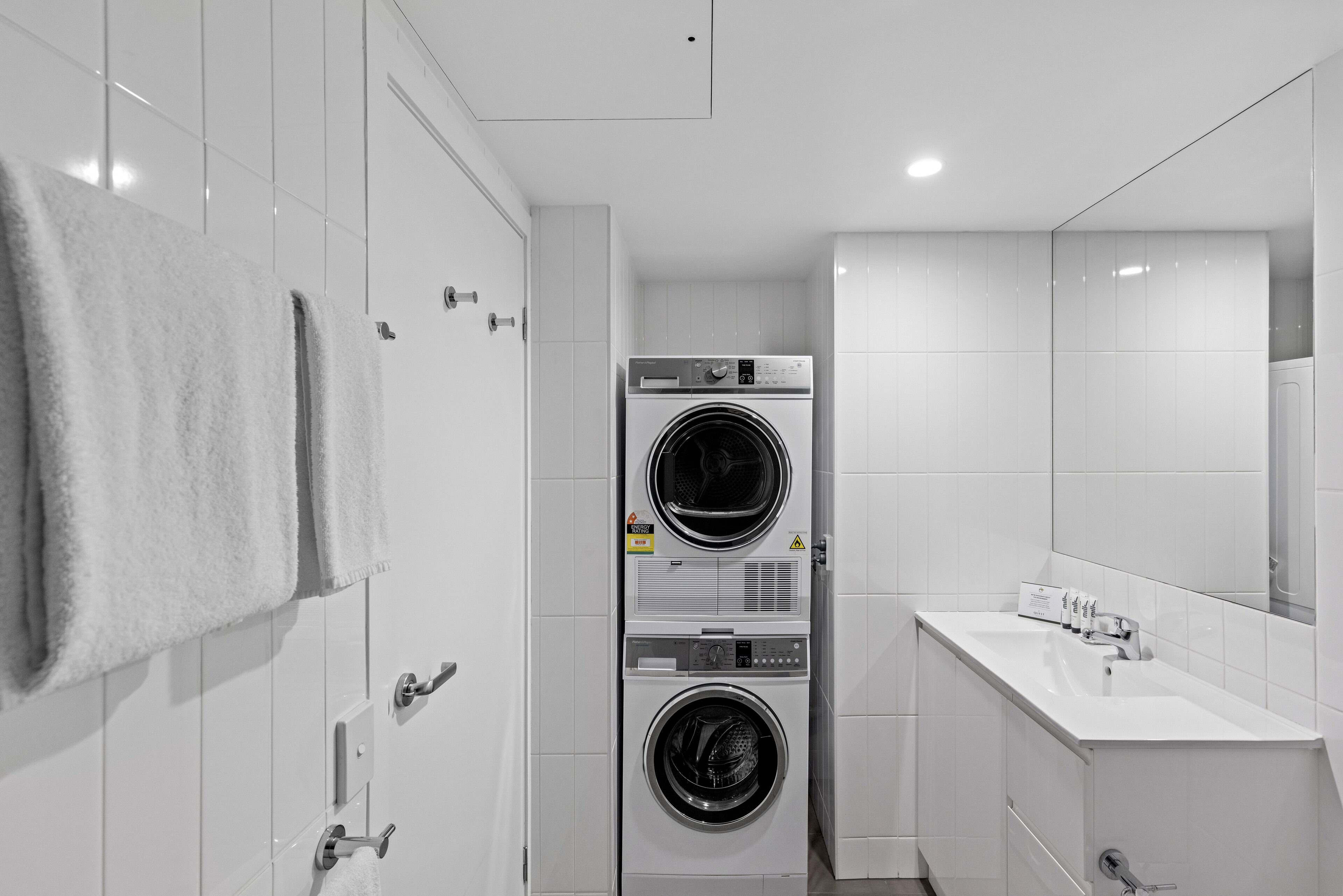 Un baño moderno con lavadora y secadora apiladas, un lavamanos y un espejo.