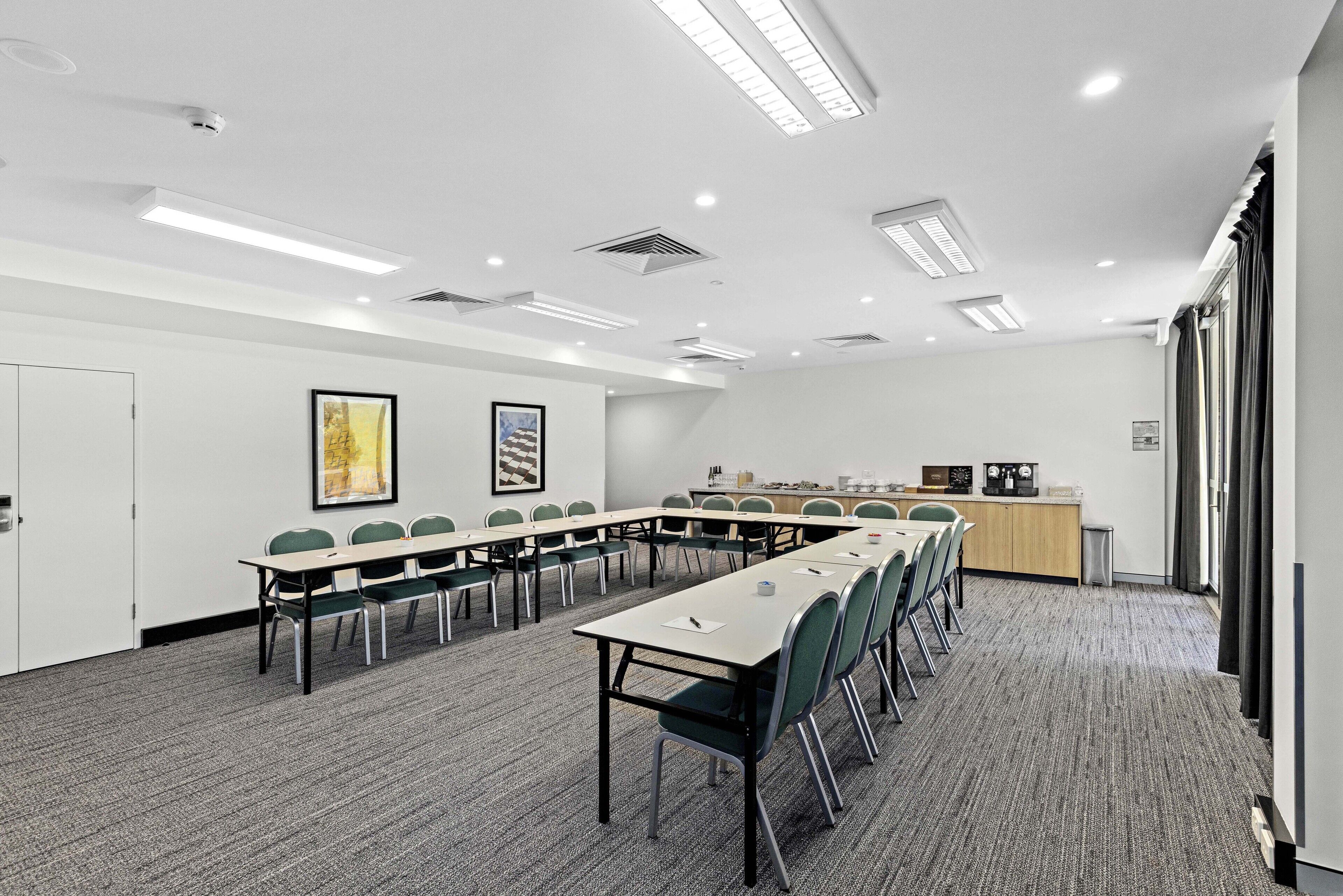 A conference room with a long table, green chairs, white walls, and a carpeted floor.