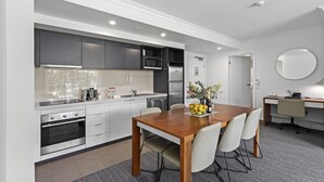 Una cocina moderna con armarios blancos, una mesa de comedor de madera y una pequeña zona de trabajo.