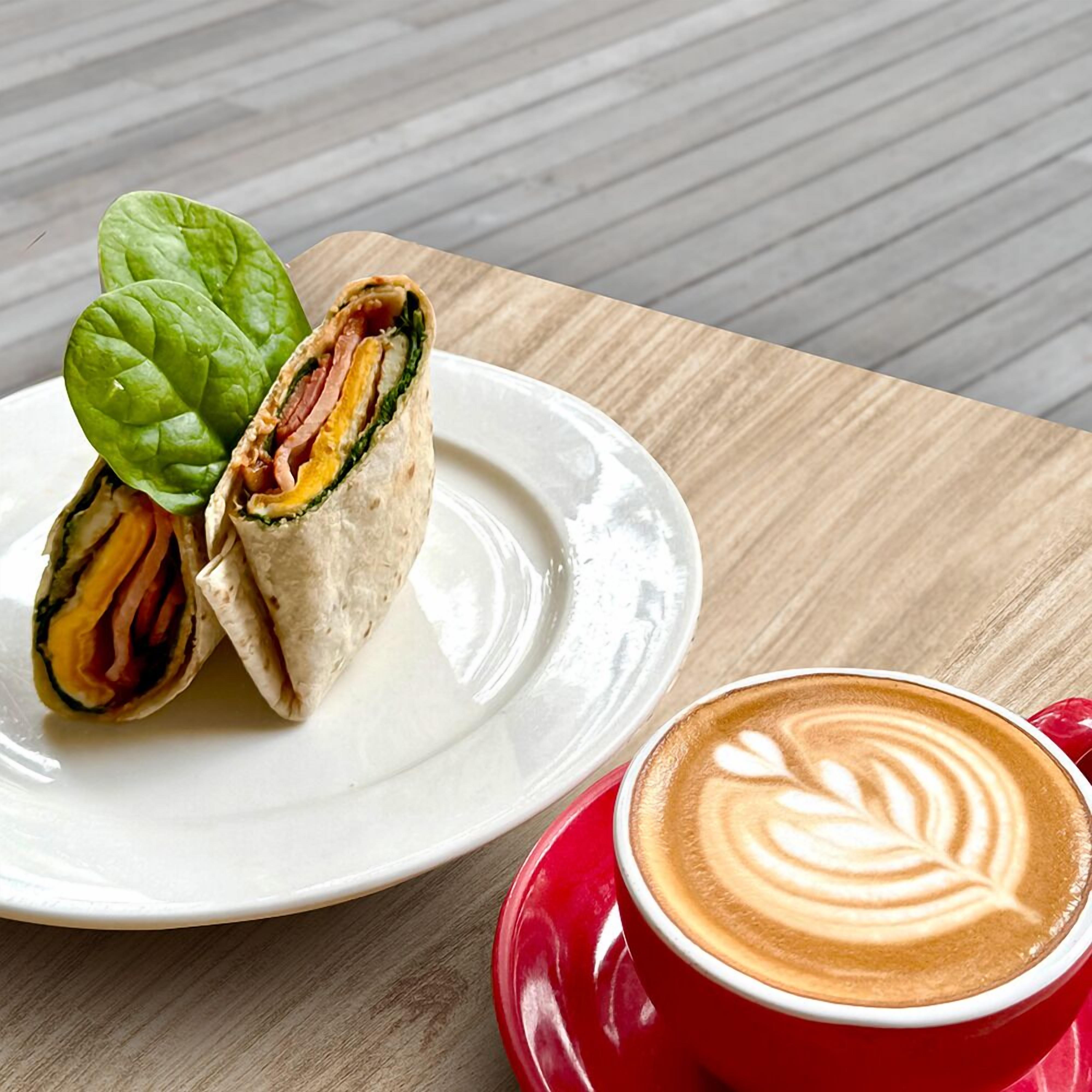 Un piatto con un panino e una tazza di caffè con decorazione in latte.