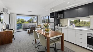 Una cocina moderna con armarios blancos, una mesa de comedor de madera y vistas a zonas verdes.