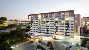 Un hotel de varios pisos con diseño moderno, con balcones en cada planta, una zona de estacionamiento techada y un patio ajardinado.