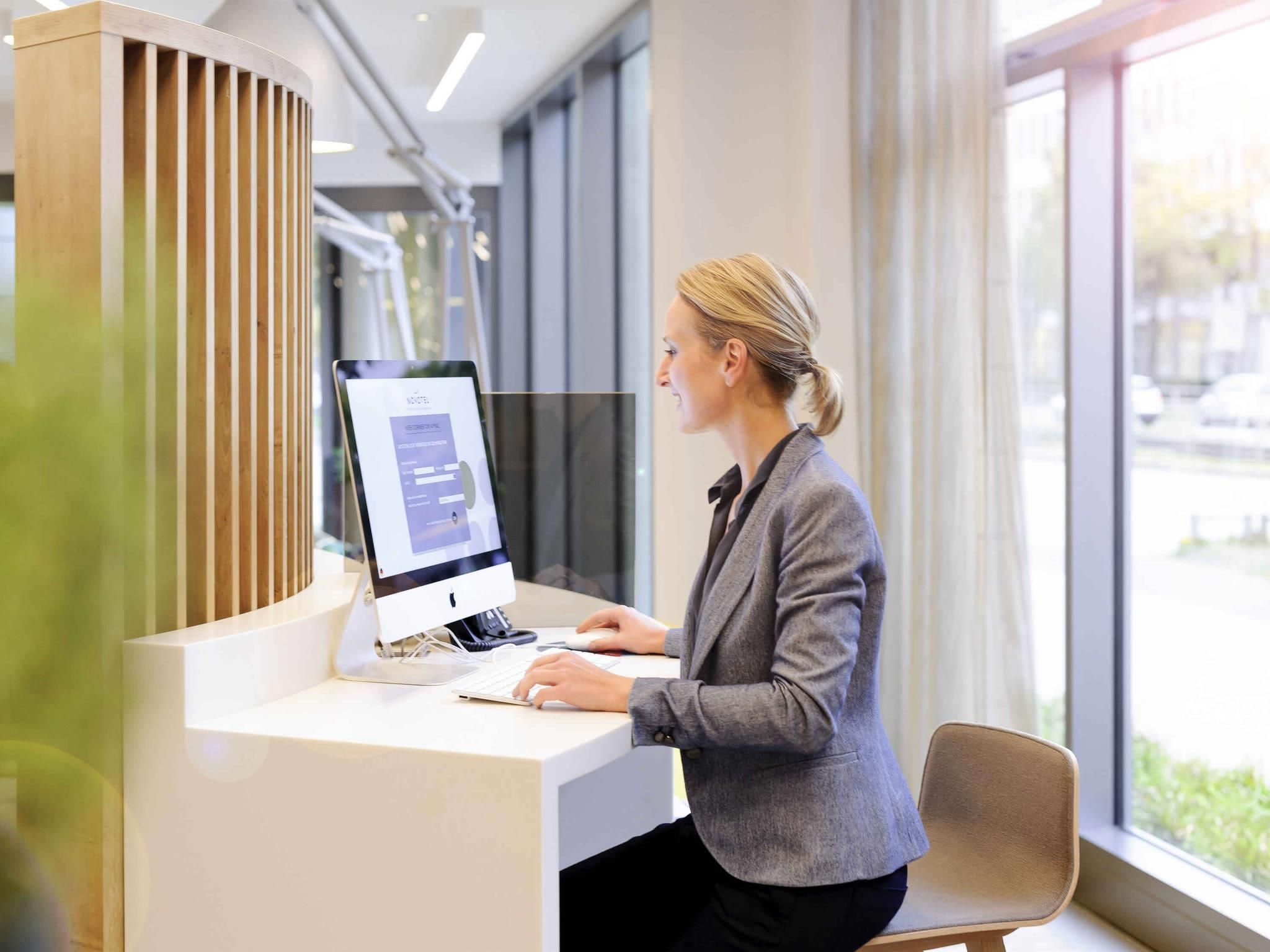 A woman at a reception desk with a computer, large windows, and a modern interior.