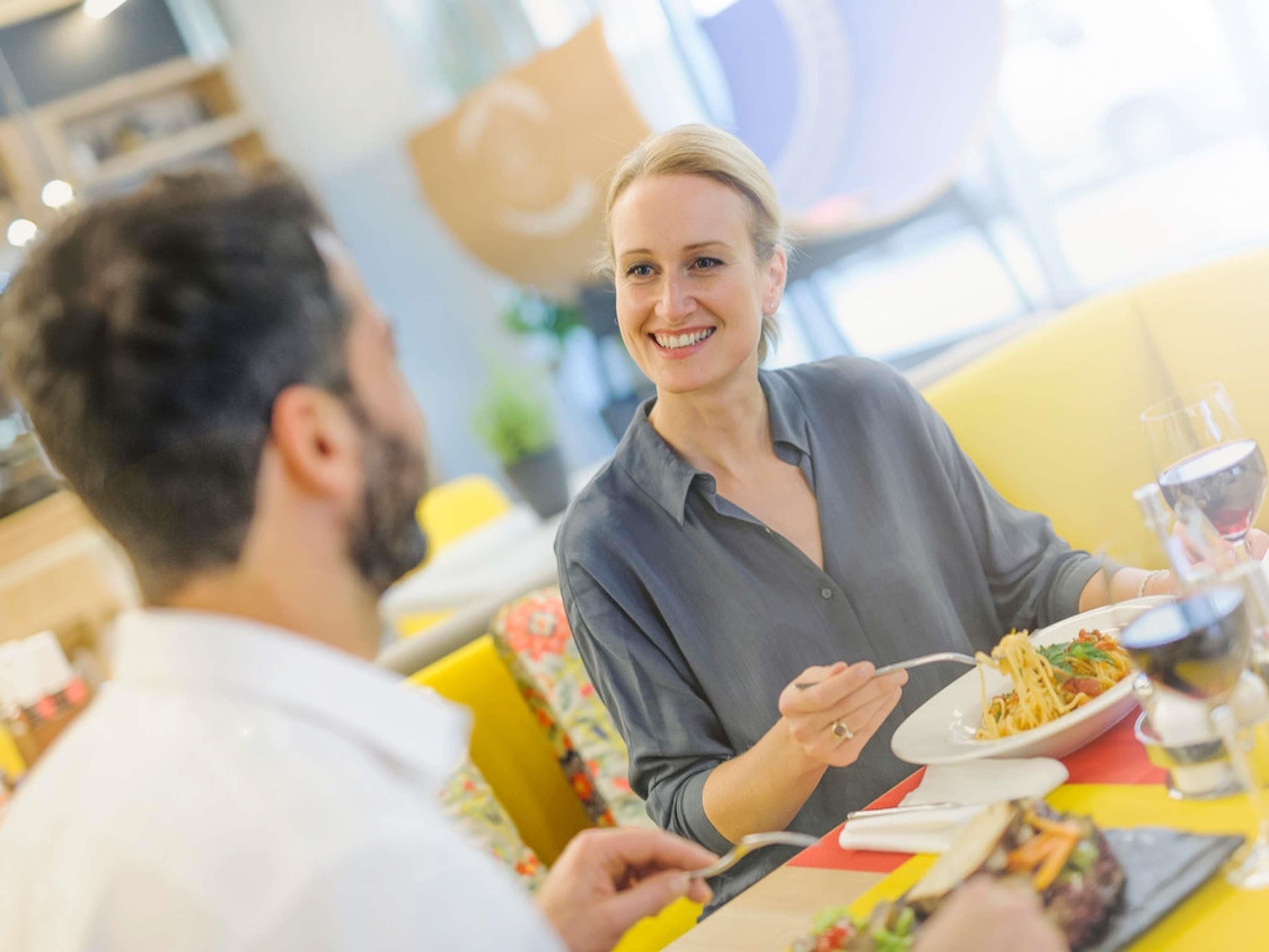 Une personne est assise à une table, devant une assiette de nourriture et un verre de vin rouge.