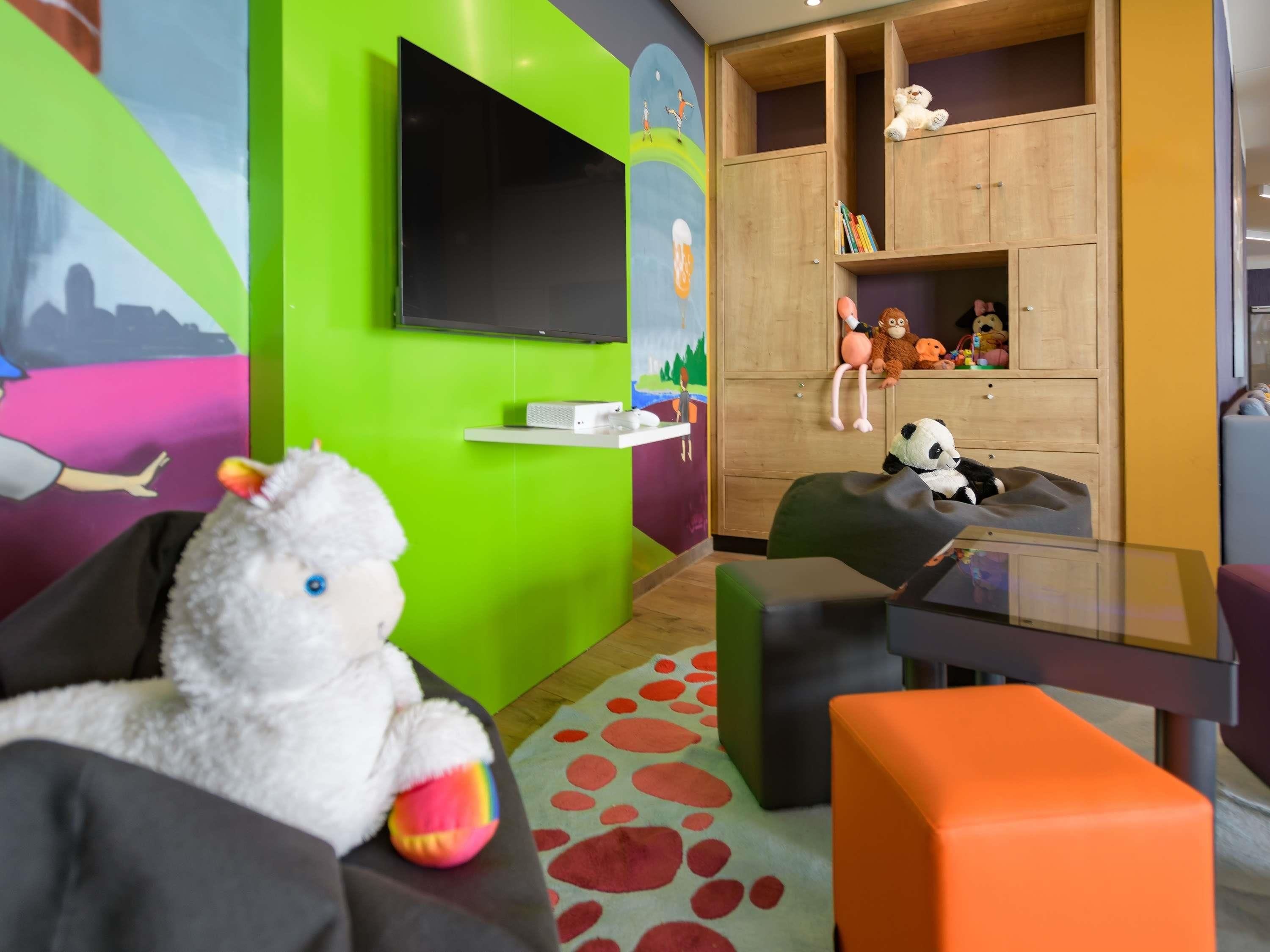 A children's playroom with a TV, bean bag chairs, a bookshelf with toys, and a colorful mural.