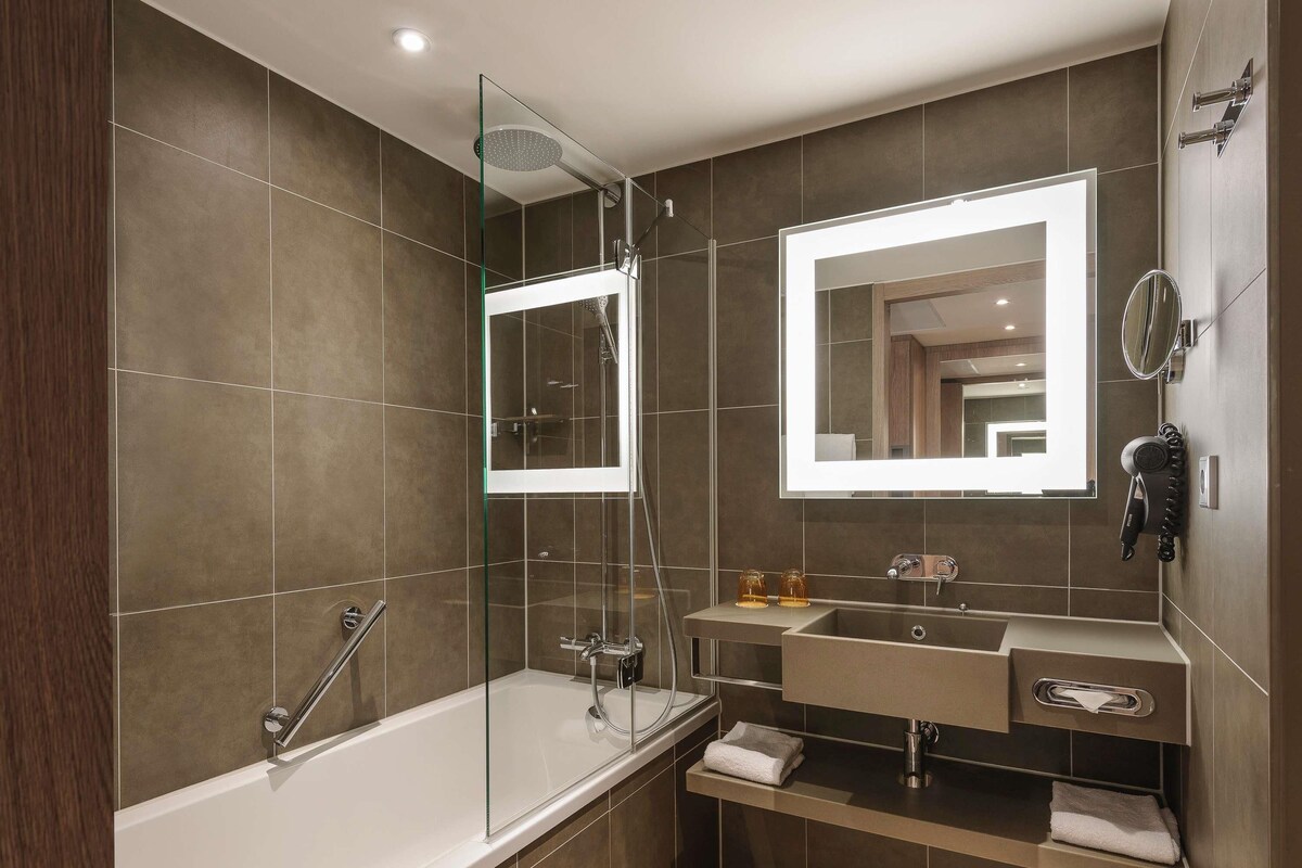 Une salle de bain moderne dotée d’une douche à parois de verre, d’un meuble-lavabo avec miroir et d’un porte-serviettes intégré.
