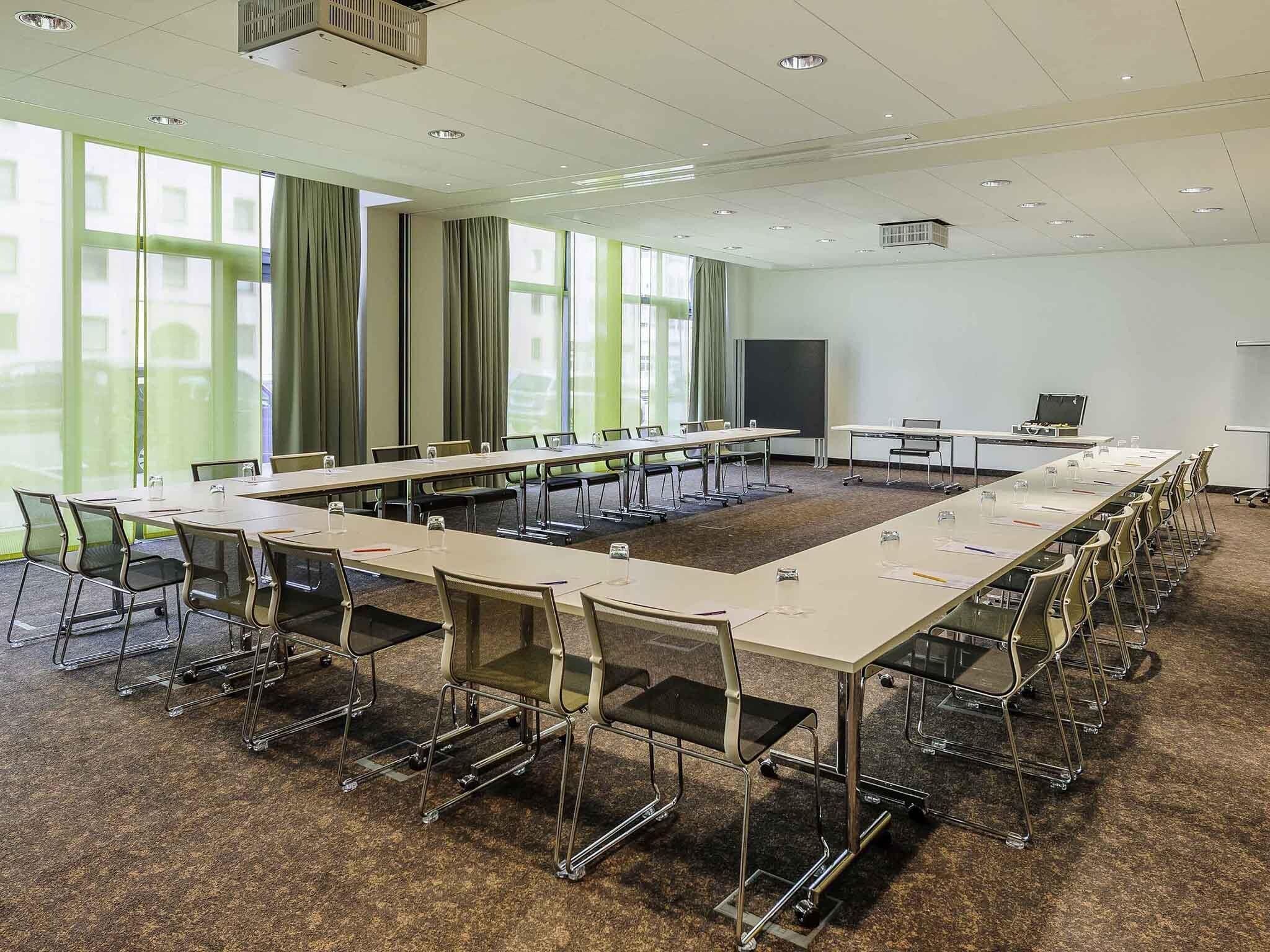 Ein Konferenzraum mit langem Tisch, Stühlen, einem Projektor und einer Whiteboard-Tafel.