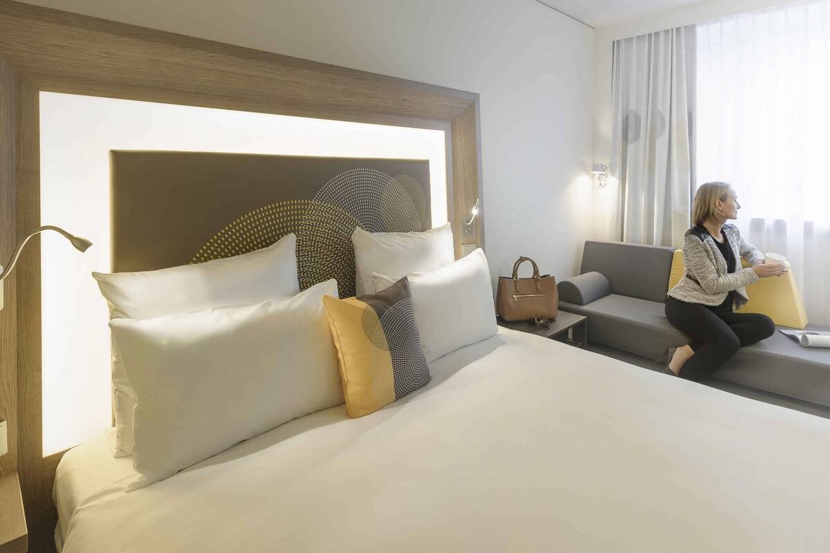 Een hotelkamer met een groot bed, een bank, een nachtkastje en een raam met gordijnen.