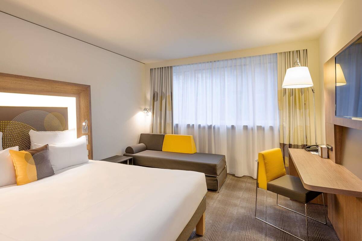 Een hotelkamer met een bed, een slaapbank, een bureau, een stoel, een televisie en een raam met gordijnen.