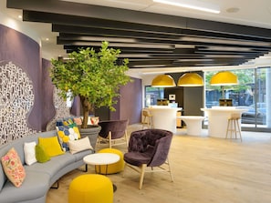 Un intérieur moderne avec un canapé aux lignes courbes, une grande plante en pot et un comptoir d’accueil équipé d’un ordinateur.