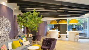 Un intérieur moderne avec un canapé aux lignes courbes, une grande plante en pot et un comptoir d’accueil équipé d’un ordinateur.