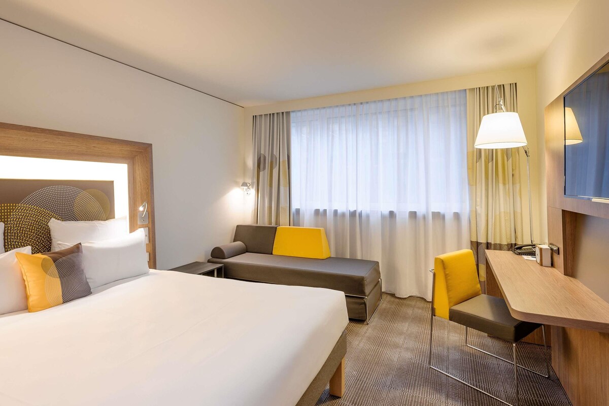 Une chambre d’hôtel équipée d’un lit, d’un canapé, d’un bureau, d’une chaise, d’une télévision et d’une fenêtre avec des rideaux.