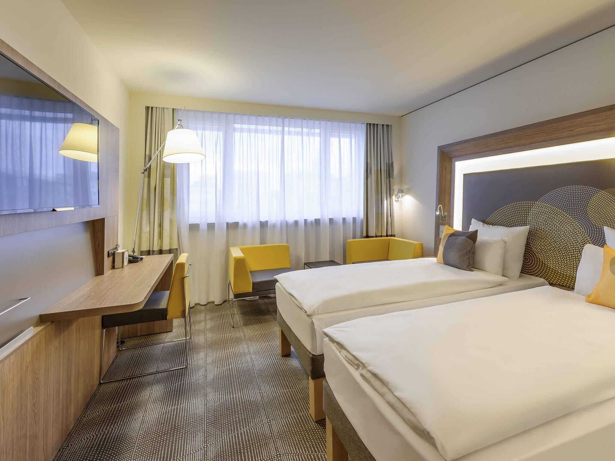 A hotel room with two beds, a desk, a chair, a TV, and a window with curtains.