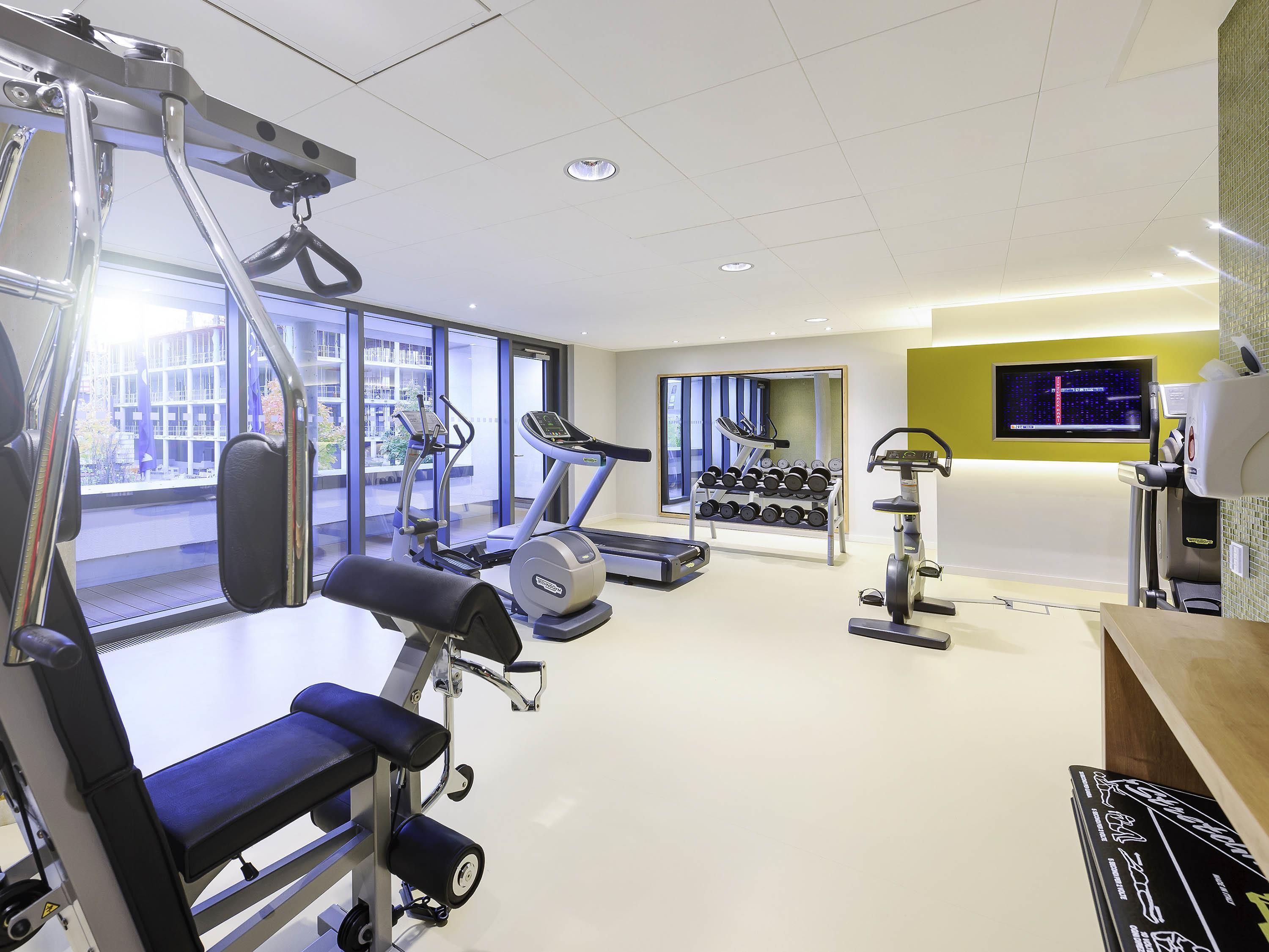 Een moderne sportschool met diverse fitnessapparaten, grote ramen en een televisie aan de muur.