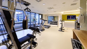 A modern gym with various exercise equipment, large windows, and a bright interior. - Novotel München City Arnulfpark (Munich)