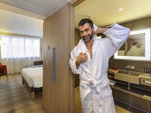 Una habitación de hotel con una cama, un armario de madera, un baño con espejo y artículos de aseo.