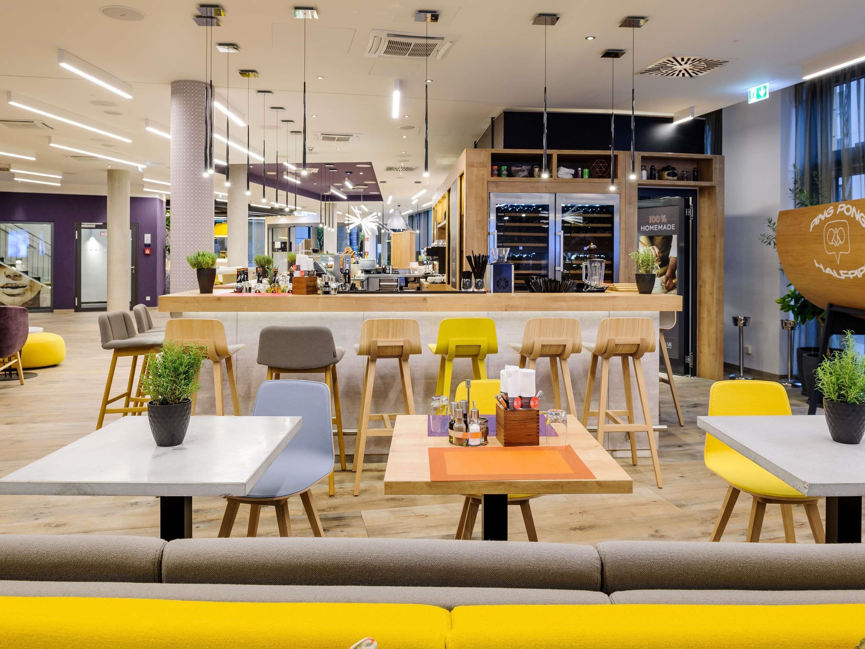 A modern cafe with a bar area, seating with tables and chairs, and a view of the city at night.