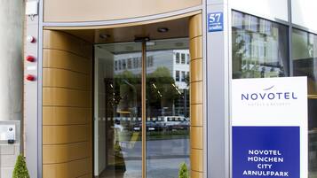 Het uiterlijk van het Novotel hotel met een gebogen entree, glazen deuren en een bord met het adres.