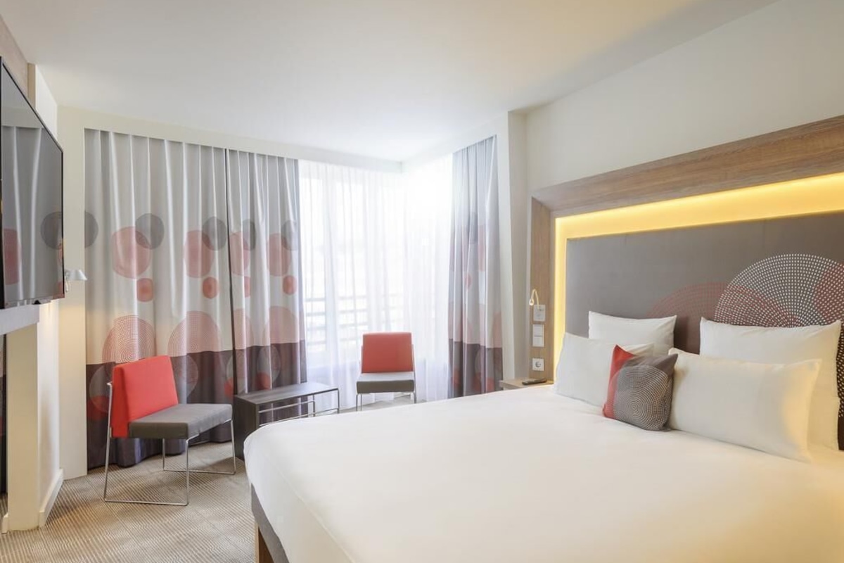A hotel room with a large bed, a desk, a chair, and a TV.