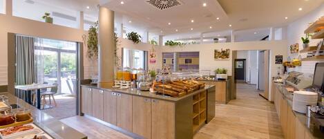Una cocina de hotel moderna con una isla central, barra para desayunos y diversas estaciones de comida.