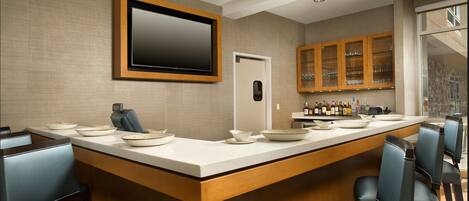 A modern kitchen with a bar area, featuring a large TV, wooden cabinets, and bar stools.