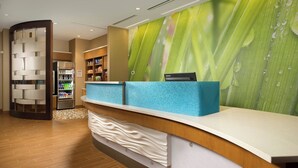 A reception area with a wooden reception desk, a blue counter, and a wall with a green leaf pattern. - SpringHill Suites Bridgeport Clarksburg (Bridgeport)
