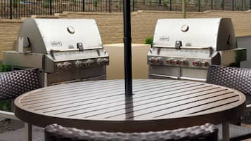 A round metal table with a grill in the center, surrounded by wicker chairs.