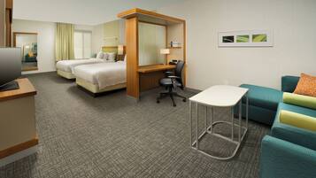 A hotel room with two beds, a desk, a chair, a TV, and a sofa.