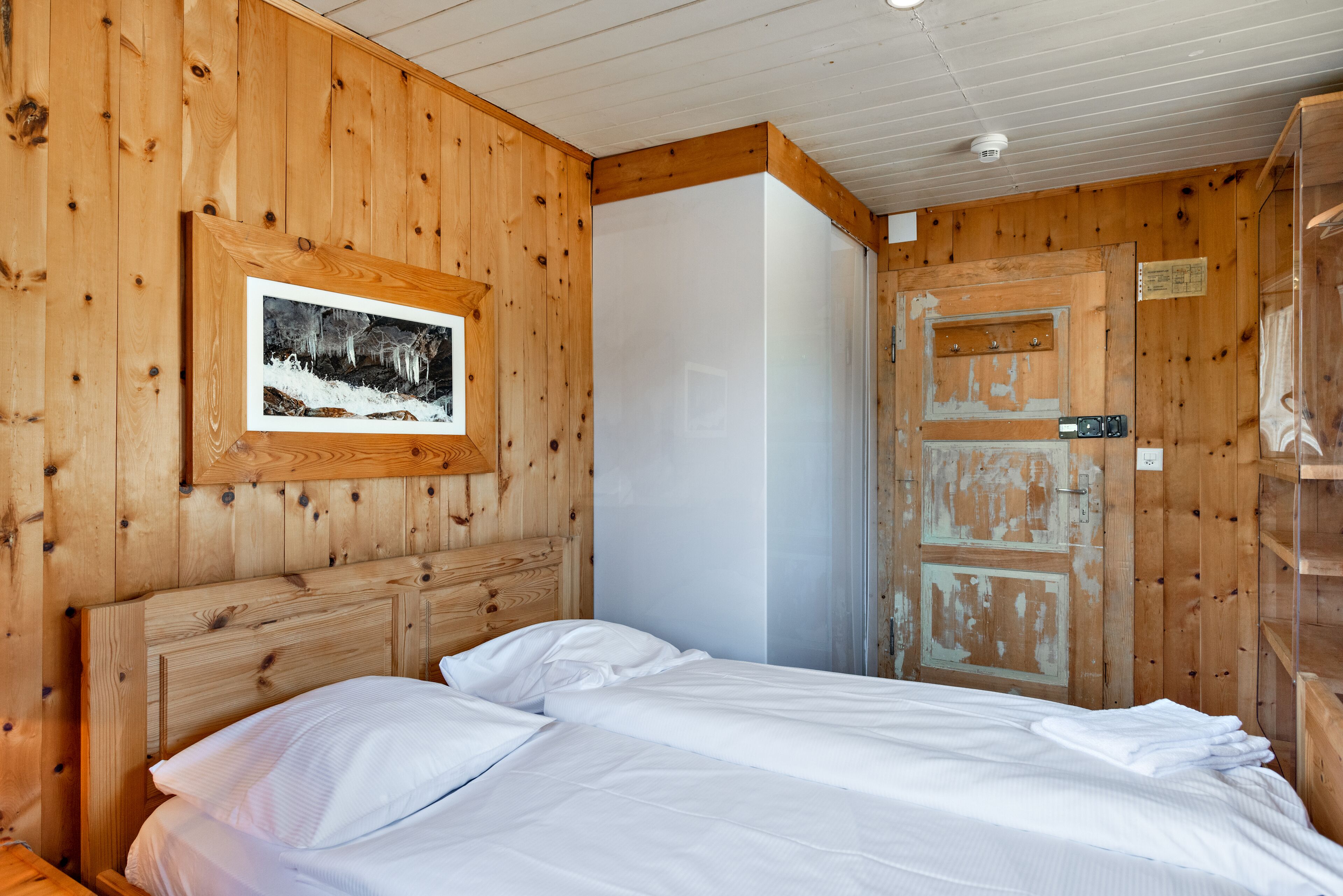 A wooden-paneled room with a bed, a framed picture on the wall, and a door with a rustic design.