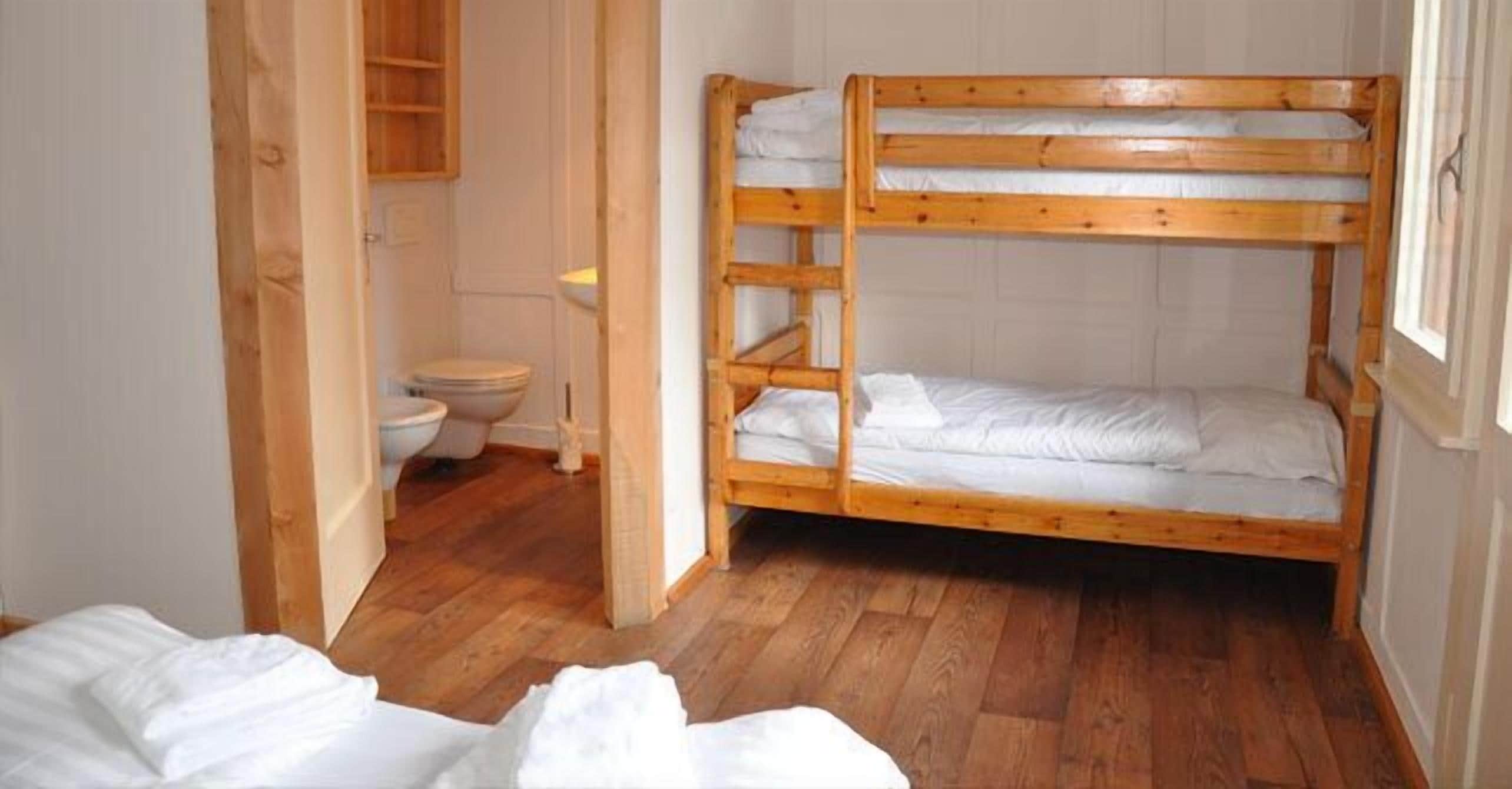 Une chambre avec des lits superposés, un plancher en bois, une porte en bois et des toilettes blanches.