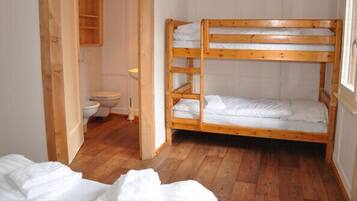 Une chambre avec des lits superposés, un plancher en bois, une porte en bois et des toilettes blanches.
