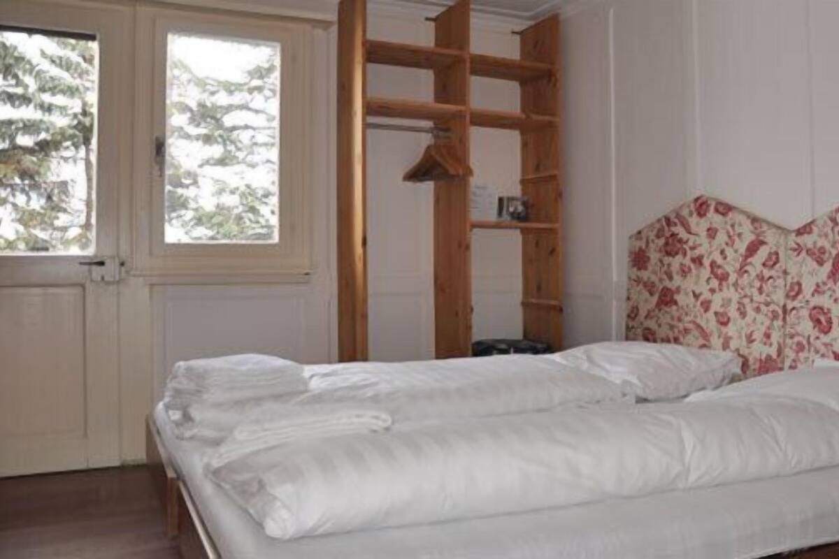 Een slaapkamer met een bed, een houten plankunit en een raam met uitzicht op bomen.