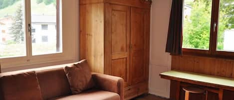 Una habitación con un armario de madera, un sofá marrón y una pequeña mesa.