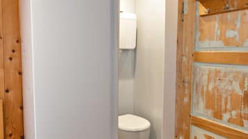 A compact bathroom with a wooden floor, a white toilet, and a wooden door with peeling paint.