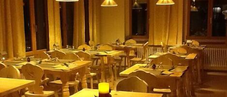 Un restaurante con varias mesas y sillas, iluminación cálida y ventanas amplias.
