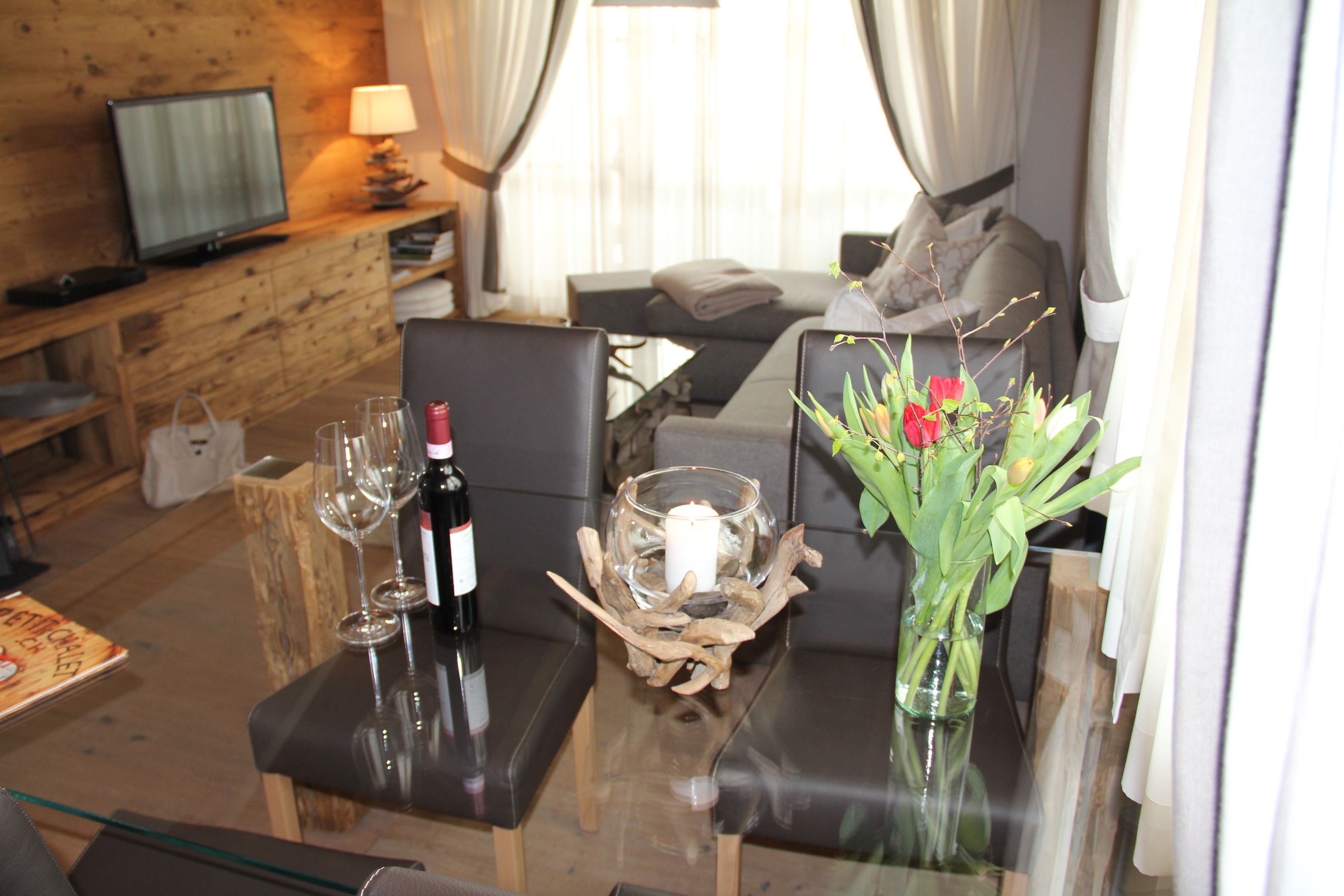 A hotel room with a glass table, a television, a sofa, and a vase with flowers.