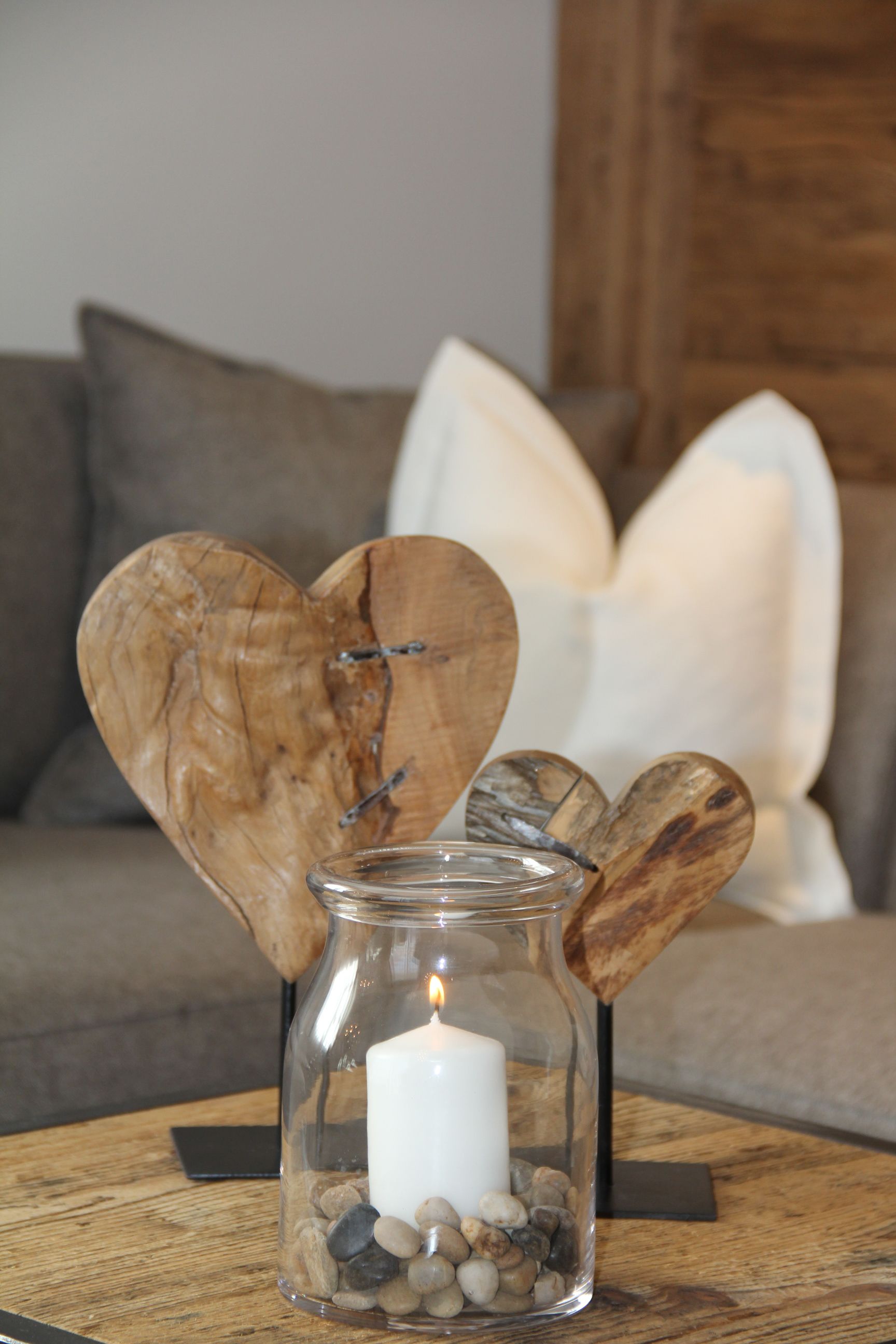 A glass candle holder with a lit candle, surrounded by smooth stones, placed on a wooden table.