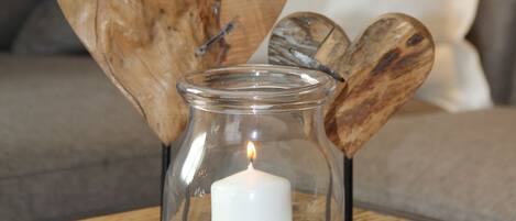 A glass candle holder with a lit candle, surrounded by smooth stones, placed on a wooden table.