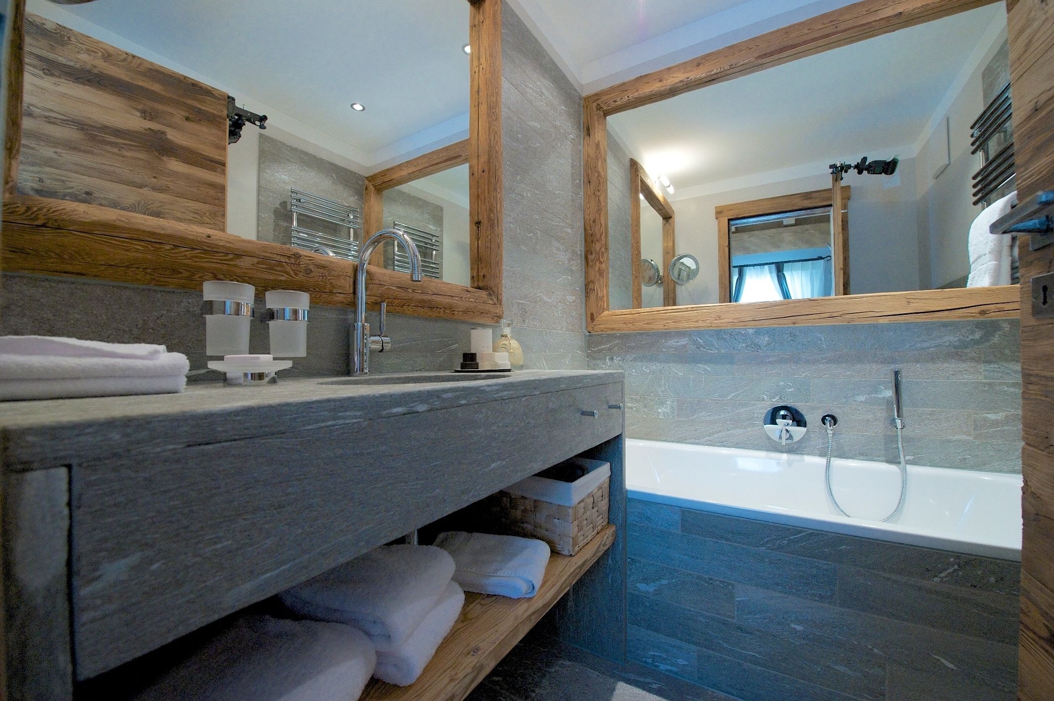 Ein modernes Badezimmer mit Waschtisch aus Holz, einem großen Spiegel, einer Badewanne und einem Handtuchhalter.
