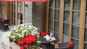 A patio area with a round table, chairs, a red umbrella, and a flower arrangement. - Hotelino Petit Chalet (Celerina-Schlarigna)