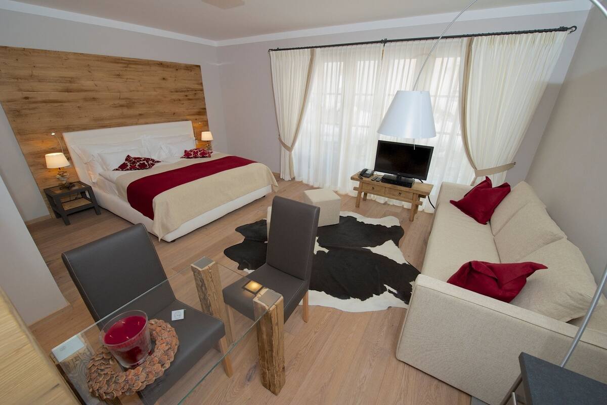 Habitación de hotel con cama, sofá, televisor y una pequeña mesa con una bebida.