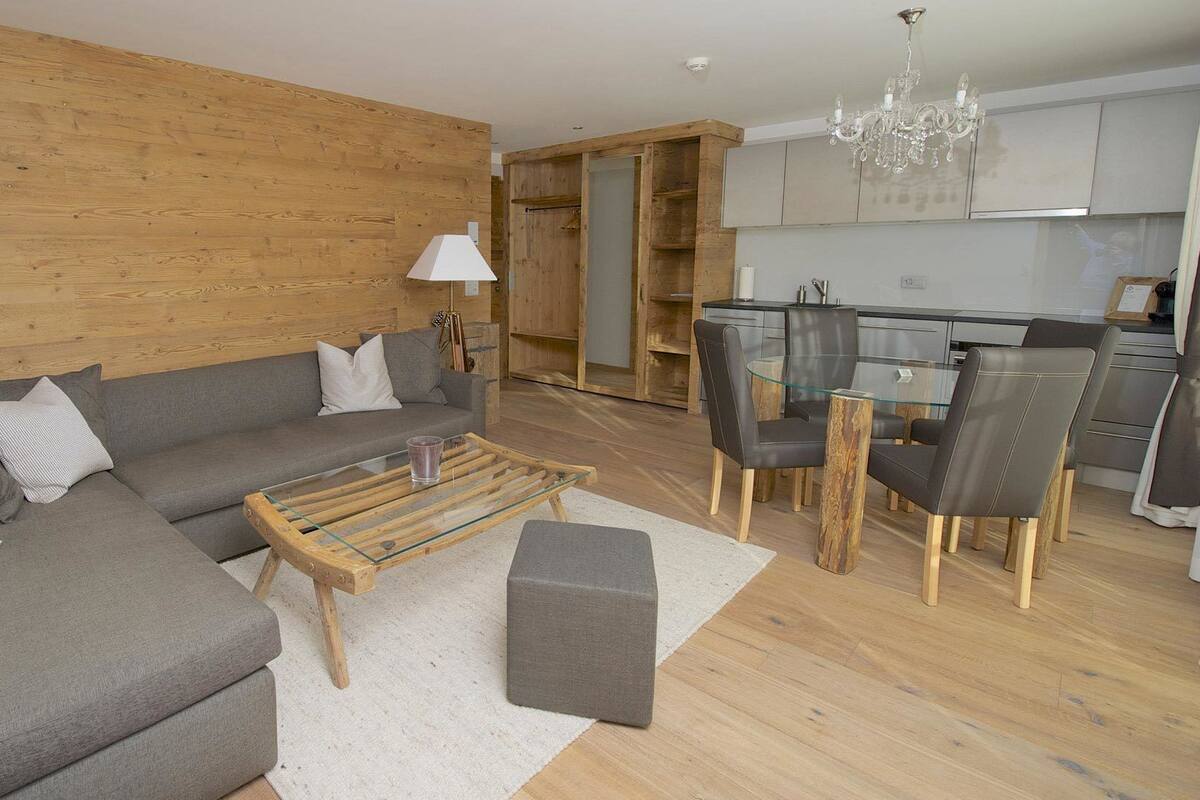 Una sala de estar moderna con un sofá gris, una mesa de centro de vidrio y un comedor con una mesa y sillas de vidrio.