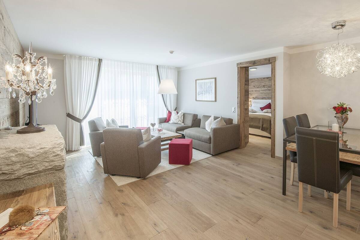 Una sala de estar moderna con comedor, que incluye una araña, chimenea y vistas de la ciudad.