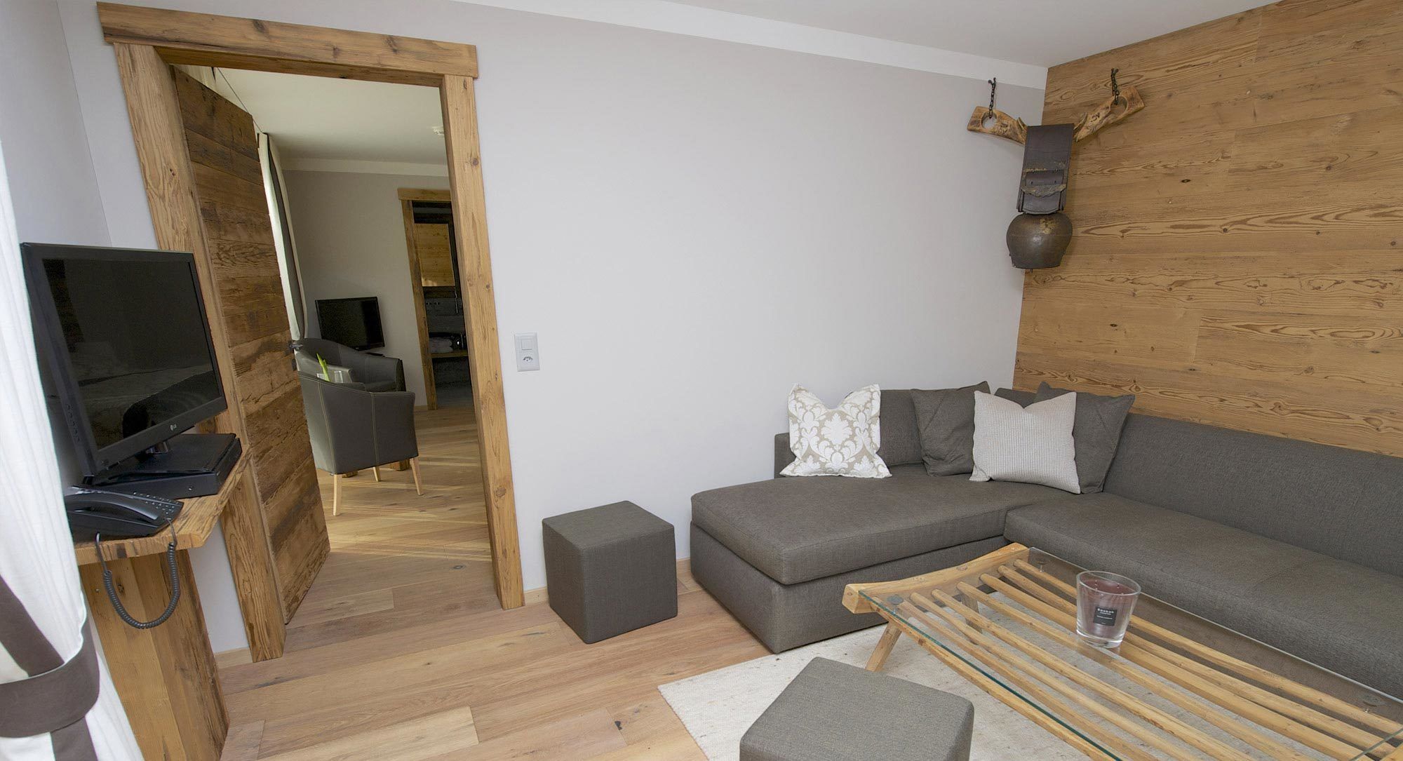 Una sala moderna con un sofá gris, una mesa de centro de cristal y un mueble de televisión de madera.